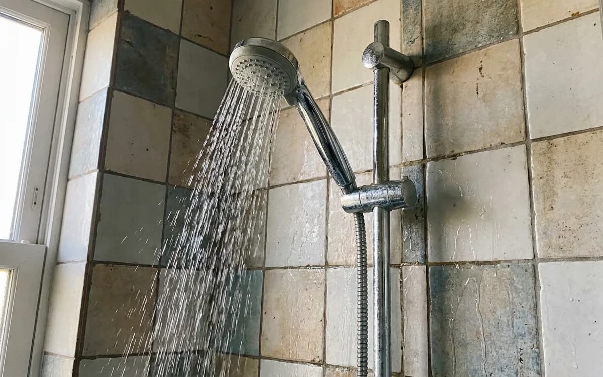 Shower fixture with water running against tiled wall