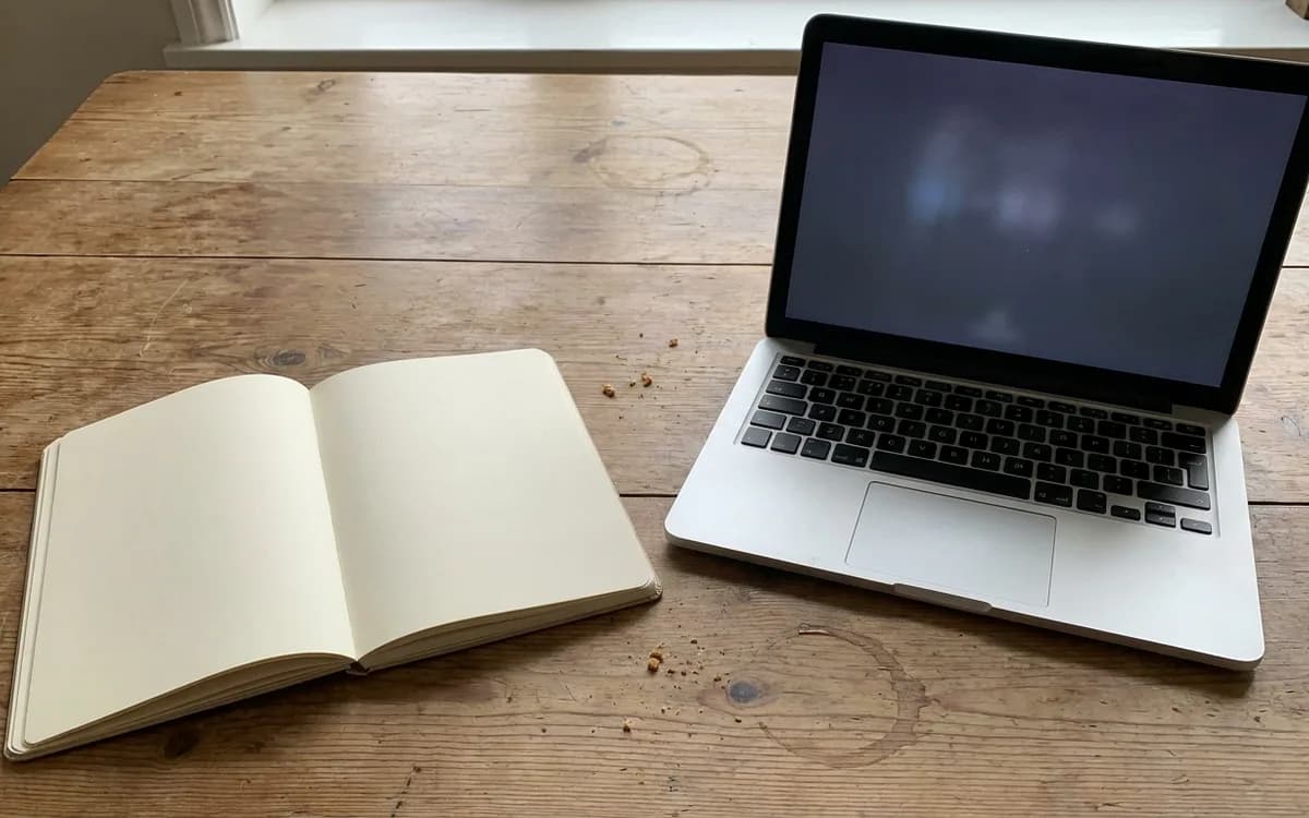 Blank notebook and a laptop with an unreadable screen on a table
