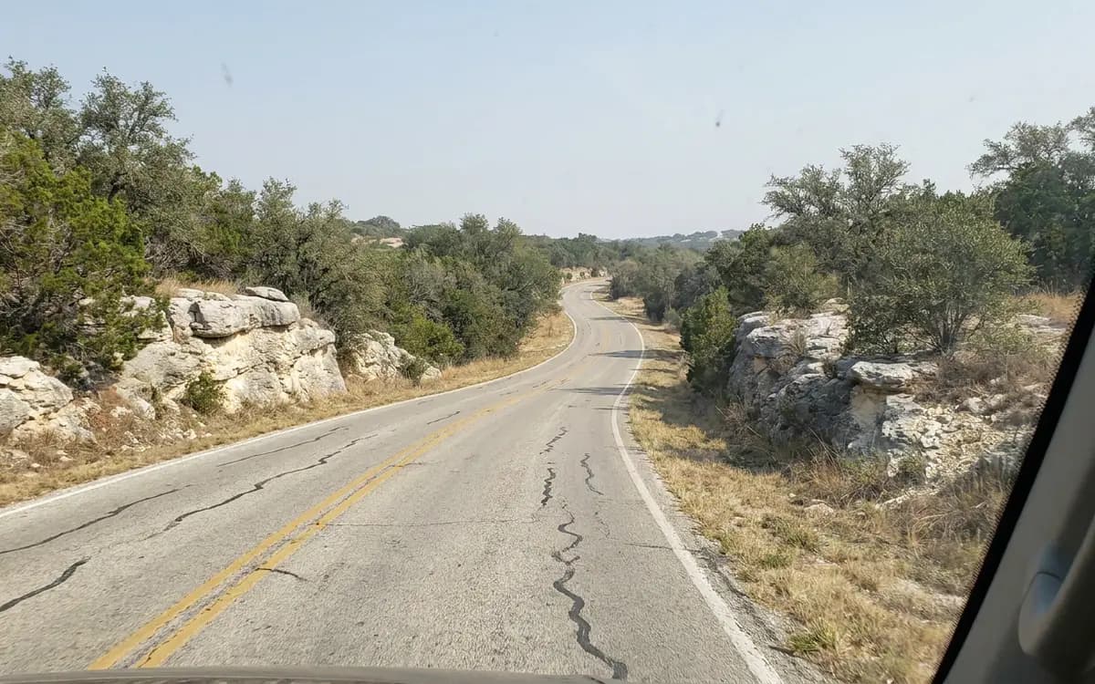 Two-lane road winding through Hill Country terrain with limestone outcrops